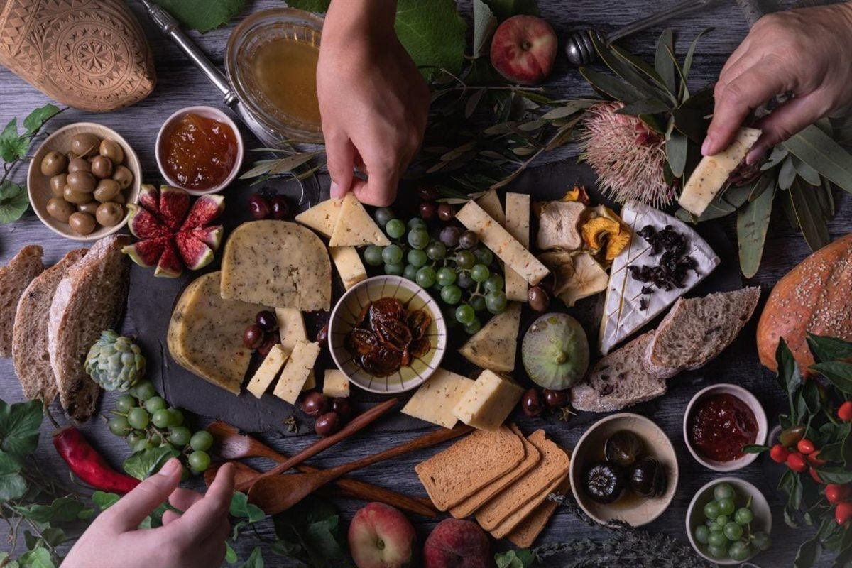 An overhead view of a large grazing platter piled with Van Gaalen cheeses, cured meats and accompaniments, hands reaching in to share